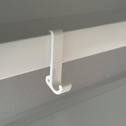 Ein robuster Multifunktionshaken in weiß, eingehängt an einem Schrank im VW Grand California. Am unteren Haken hängt eine Jacke, während durch die kleine Öse auf der Rückseite eine Schnur gezogen ist, an der ein Bluetooth-Lautsprecher befestigt wurde. Der Haken fügt sich unauffällig ins Fahrzeugdesign ein und bleibt sowohl bei geöffnetem als auch geschlossenem Schrank nutzbar. Perfekt für mehr Ordnung im Camper!