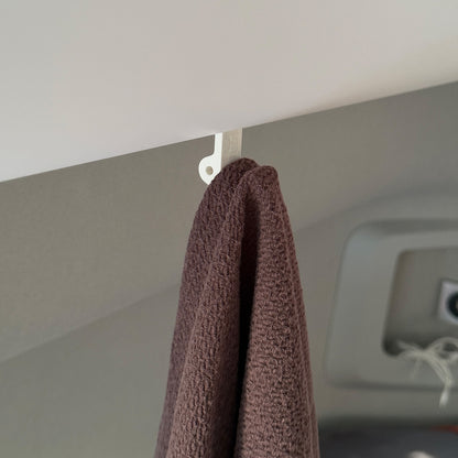 Ein robuster Multifunktionshaken in weiß, eingehängt an einem Schrank im VW Grand California. Am unteren Haken hängt eine Jacke, während durch die kleine Öse auf der Rückseite eine Schnur gezogen ist, an der ein Bluetooth-Lautsprecher befestigt wurde. Der Haken fügt sich unauffällig ins Fahrzeugdesign ein und bleibt sowohl bei geöffnetem als auch geschlossenem Schrank nutzbar. Perfekt für mehr Ordnung im Camper!