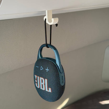 Ein robuster Multifunktionshaken in weiß, eingehängt an einem Schrank im VW Grand California. inklusive Bluetooth Lautsprecher. Am unteren Haken hängt eine Jacke, während durch die kleine Öse auf der Rückseite eine Schnur gezogen ist, an der ein Bluetooth-Lautsprecher befestigt wurde. Der Haken fügt sich unauffällig ins Fahrzeugdesign ein und bleibt sowohl bei geöffnetem als auch geschlossenem Schrank nutzbar. Perfekt für mehr Ordnung im Camper!